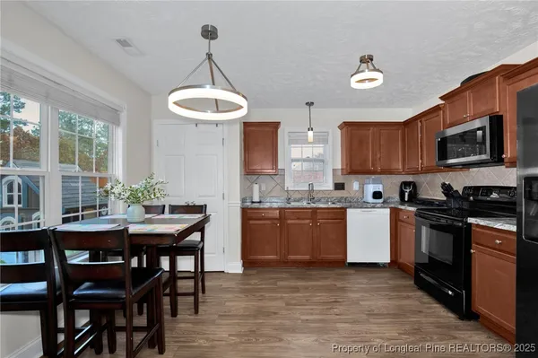 a kitchen with granite countertop wooden floors a stove a microwave a dining table and chairs