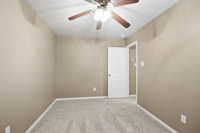 an empty room with chandelier fan and windows