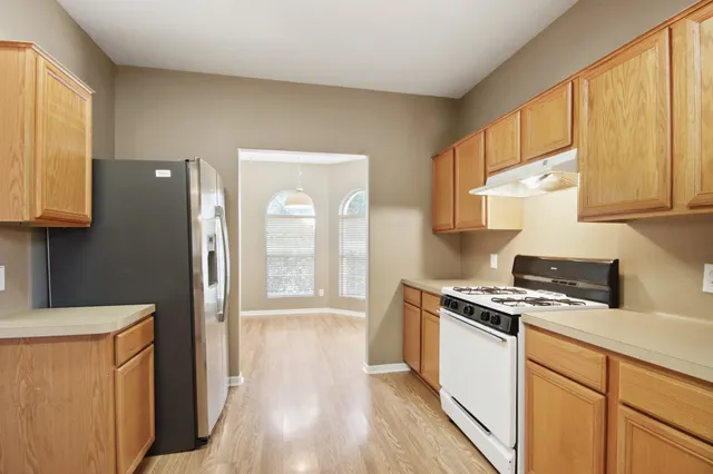 a kitchen with stainless steel appliances granite countertop a refrigerator a sink dishwasher and wooden cabinets with wooden floor