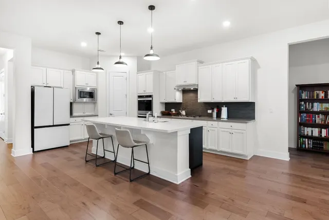 a kitchen with stainless steel appliances kitchen island granite countertop a refrigerator a stove a oven and white cabinets with wooden floor