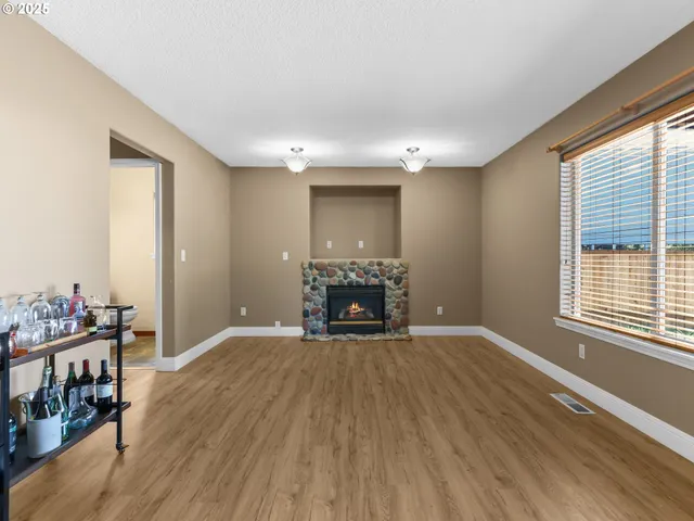 a view of an empty room with wooden floor fireplace and a window