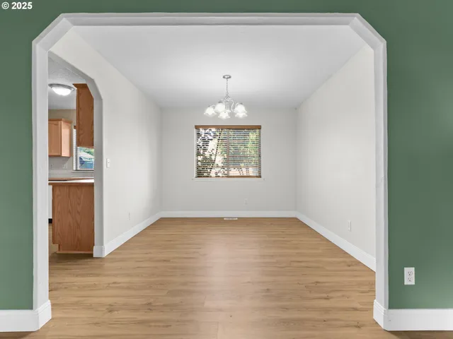 an empty room with wooden floor chandelier and windows
