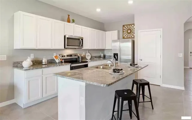 a kitchen with stainless steel appliances granite countertop a sink a microwave a refrigerator and white cabinets