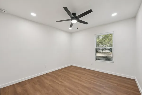an empty room with wooden floor ceiling fan and windows