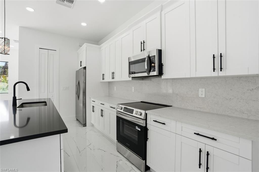 2930 20th Street Southwest Lehigh Acres, FL 33976 - Photo 13 of 43 a kitchen with stainless steel appliances white cabinets and a sink