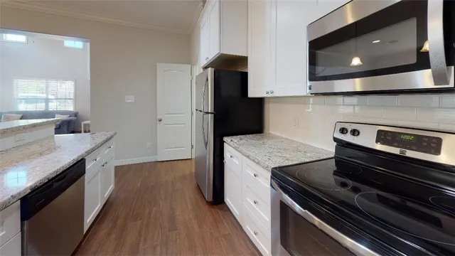 a kitchen with kitchen island granite countertop a refrigerator oven a sink and white cabinets with wooden floor