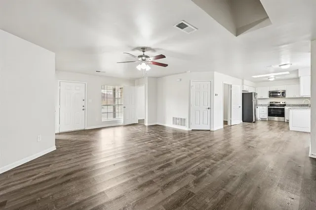 a view of an empty room with wooden floor and a ceiling fan