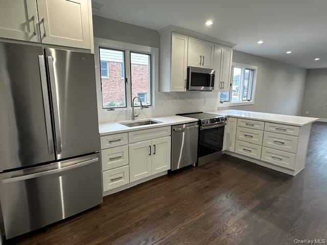 5 Linwood Road North, Unit 1 Port Washington, NY 11050 - Photo 4 of 12 Kitchen featuring stainless steel appliances, a peninsula, dark wood finished floors, white cabinetry, and decorative backsplash
