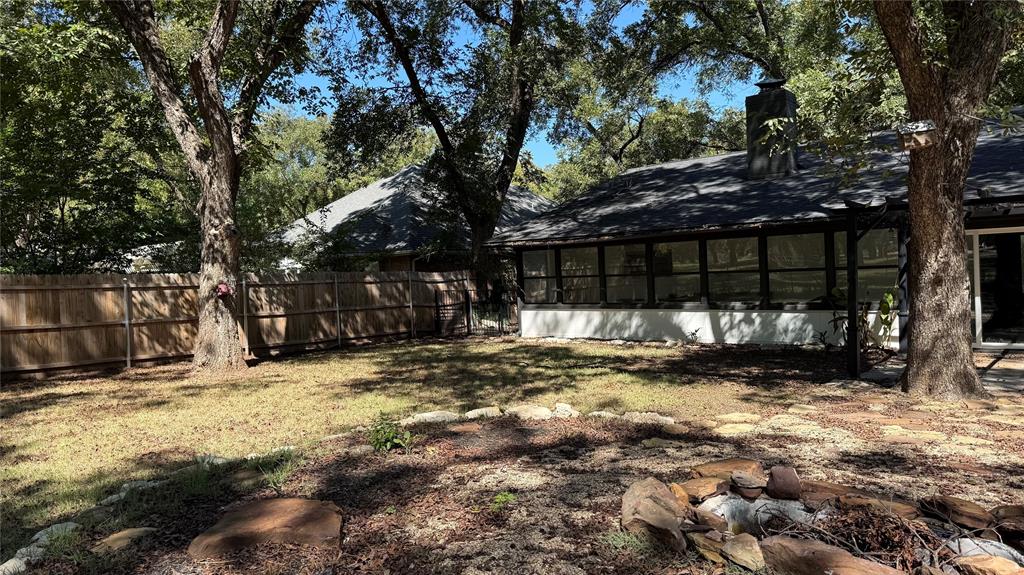8513 Ravenswood Road Granbury, TX 76049 - Photo 21 of 21 Expansive backyard featuring a wood privacy fence, mature trees, and a stone-edged fire pit area