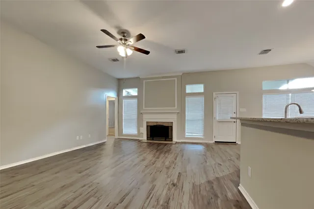 a view of a livingroom with a fireplace a ceiling fan and wooden floor