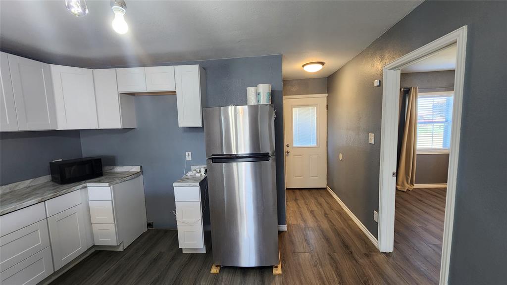 809 Bowie Street Sweetwater, TX 79556 - Photo 7 of 20 Kitchen with freestanding refrigerator, black microwave, dark wood finished floors, and white cabinetry