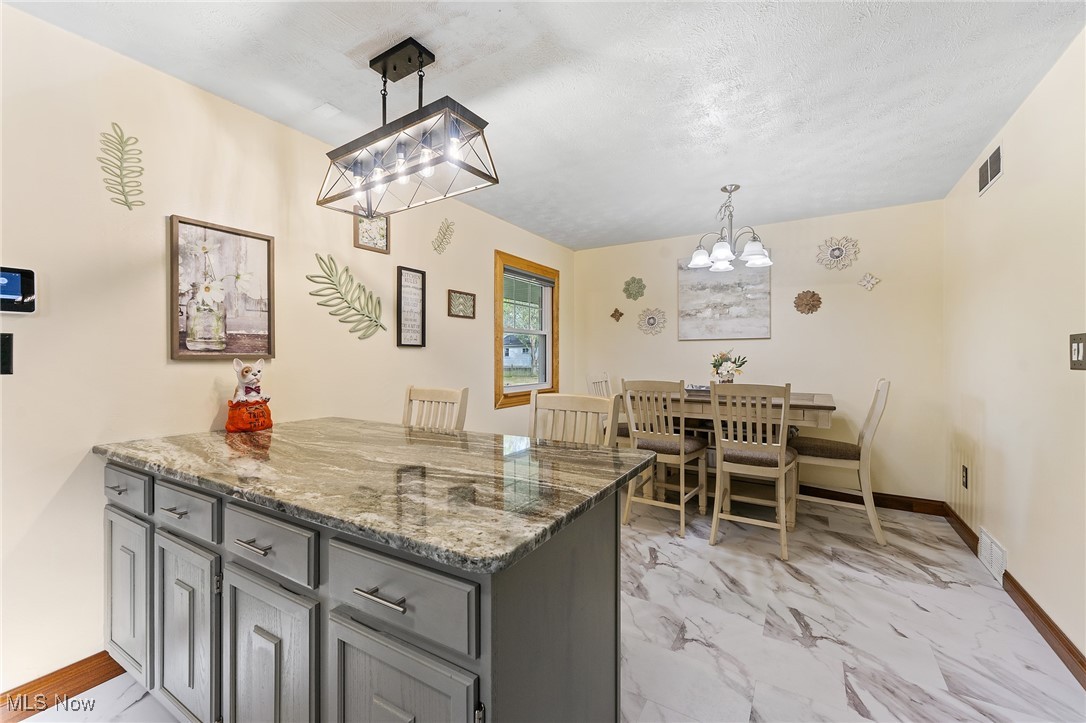 Kitchen featuring kitchen peninsula, stone countertops, a textured ceiling, an inviting chandelier, and decorative light fixtures