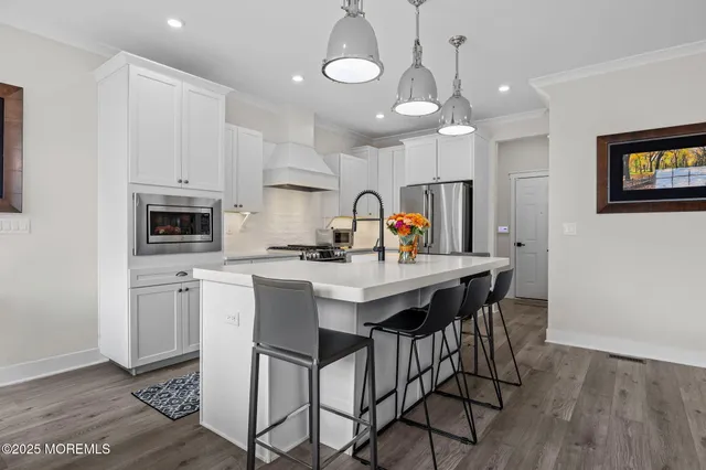 a kitchen with stainless steel appliances kitchen island granite countertop a sink a stove a refrigerator and white cabinets with wooden floor