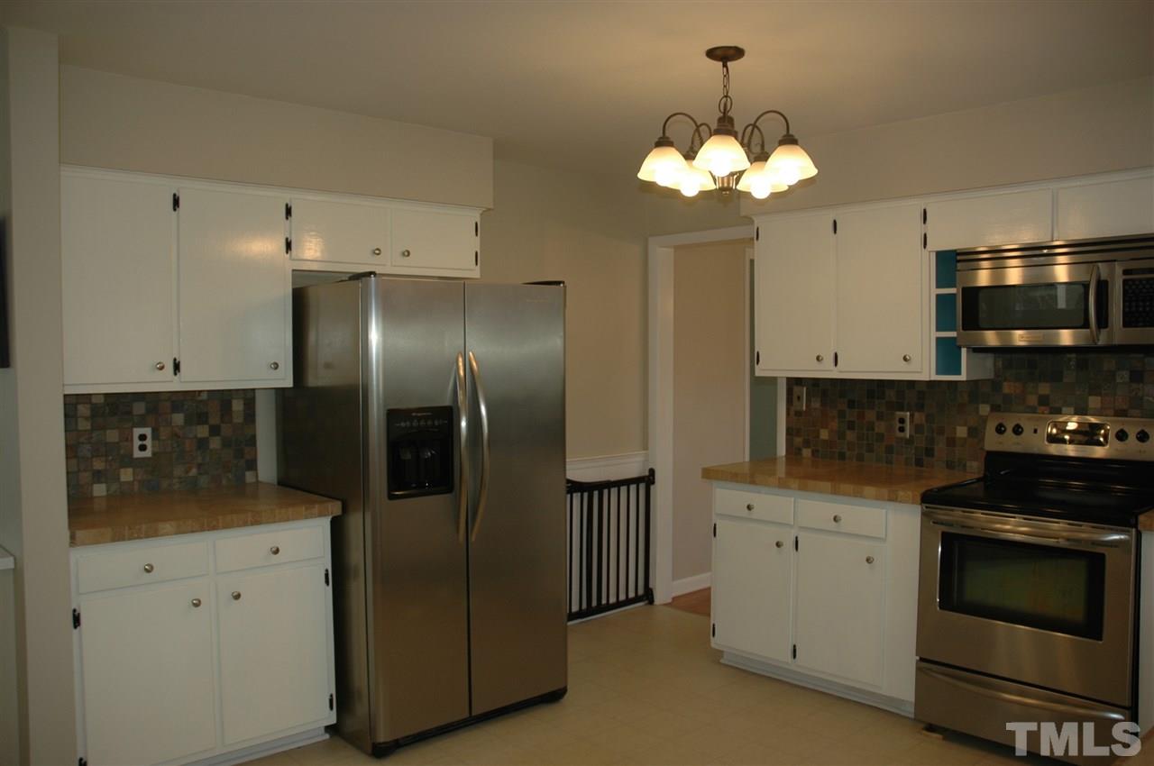 716 Currituck Drive Raleigh, NC 27609 - Photo 4 of 19 Kitchen features white cabinets, stainless steel appliances, tile backsplash & counters, & built in wine rack.