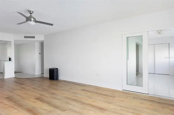 a view of an empty room with wooden floor and a ceiling fan