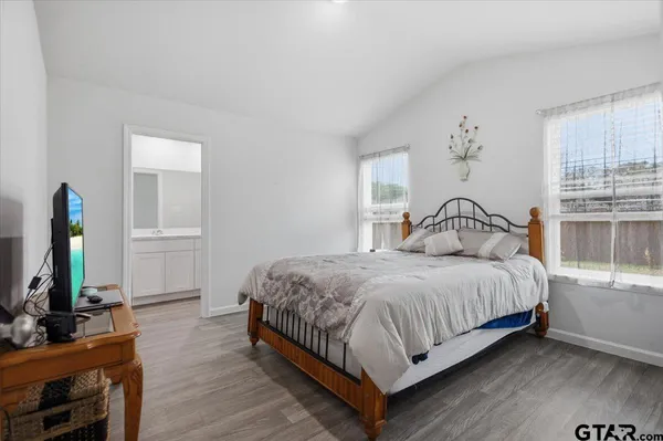 a bedroom with a bed table flat screen tv and two windows