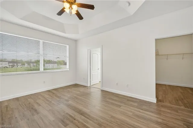 an empty room with wooden floor chandelier fan and windows