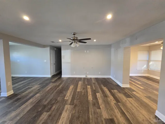 an empty room with wooden floor fan and windows