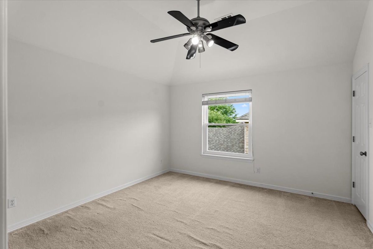2304 Village View Loop Pflugerville, TX 78660 - Photo 33 of 40 A well-lit bedroom features vaulted ceilings and plush carpeting, with a window offering views of the neighborhood.