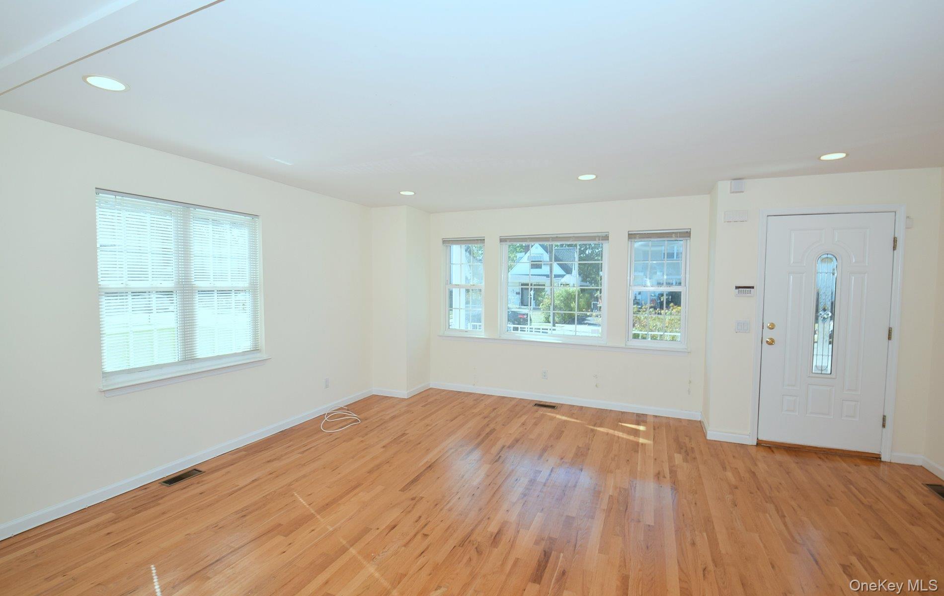 74 Firwood Road, Unit A Port Washington, NY 11050 - Photo 2 of 13 Spacious room featuring wood flooring, recessed lighting, multiple windows with blinds, a white entry door with an arched glass insert, and light-colored wall finishes