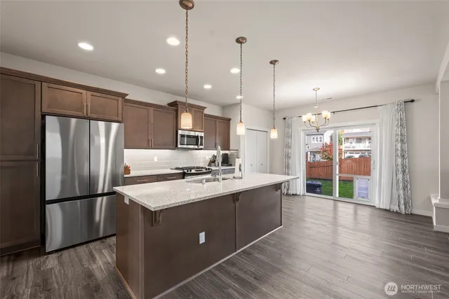 a kitchen with stainless steel appliances granite countertop a refrigerator a sink dishwasher a stove and white cabinets with wooden floor