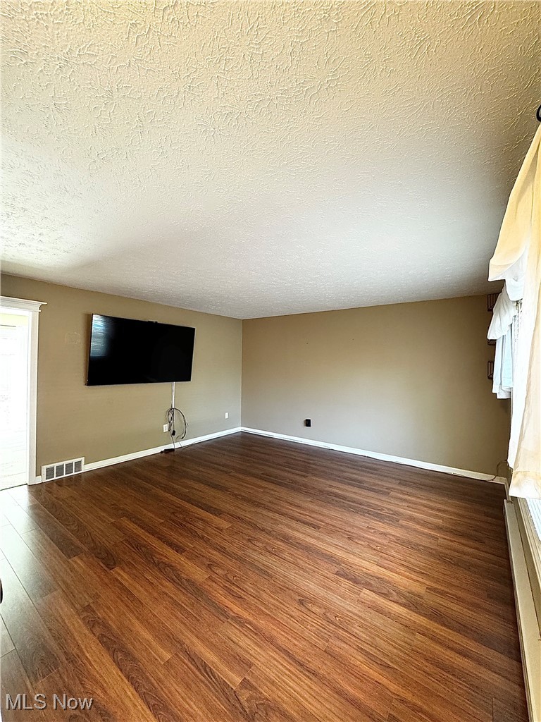 Unfurnished living room with dark wood-style floors and a textured ceiling