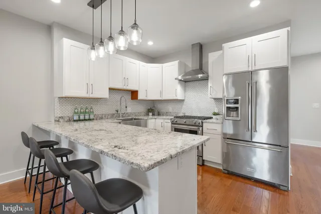 a kitchen with granite countertop a refrigerator a stove a kitchen island and chairs with wooden floor