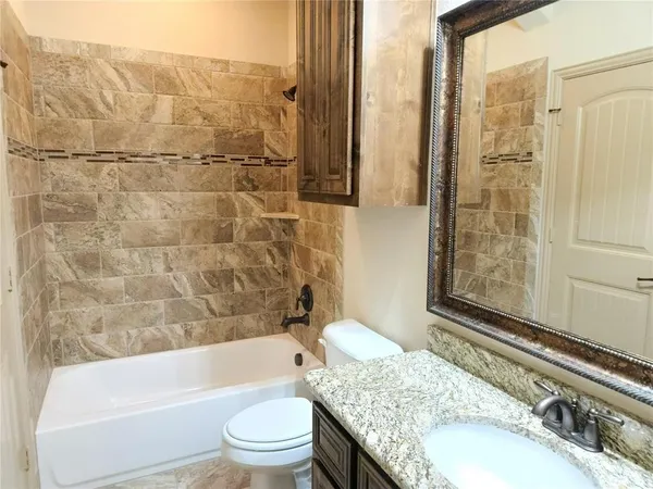 a bathroom with a granite countertop bathtub shower sink vanity and toilet