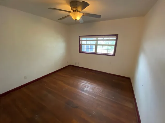 an empty room with wooden floor fan and windows