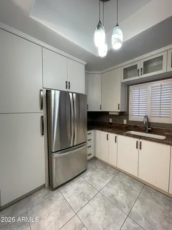 a kitchen with granite countertop a refrigerator a sink and white cabinets