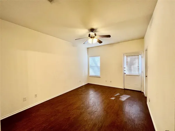 a view of an empty room with wooden floor and a ceiling fan