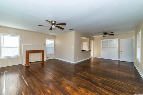 an empty room with wooden floor chandelier fan and windows