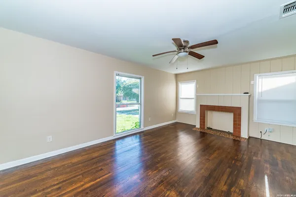 an empty room with wooden floor a ceiling fan and windows