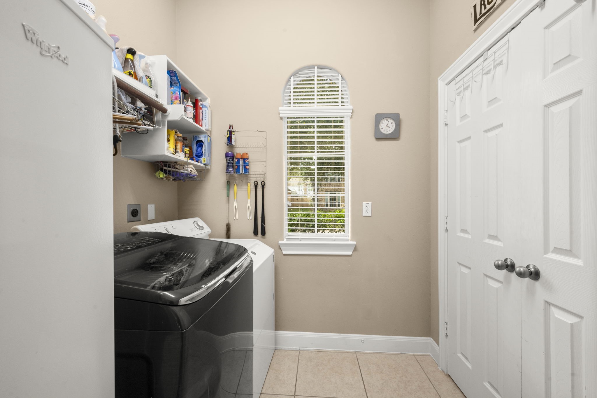 6315 Amelia Springs Drive Spring, TX 77379 - Photo 19 of 46 A tidy laundry room featuring shelving for storage, and a window with natural light. It has a neutral color scheme with shelves for well-organized cleaning supplies.