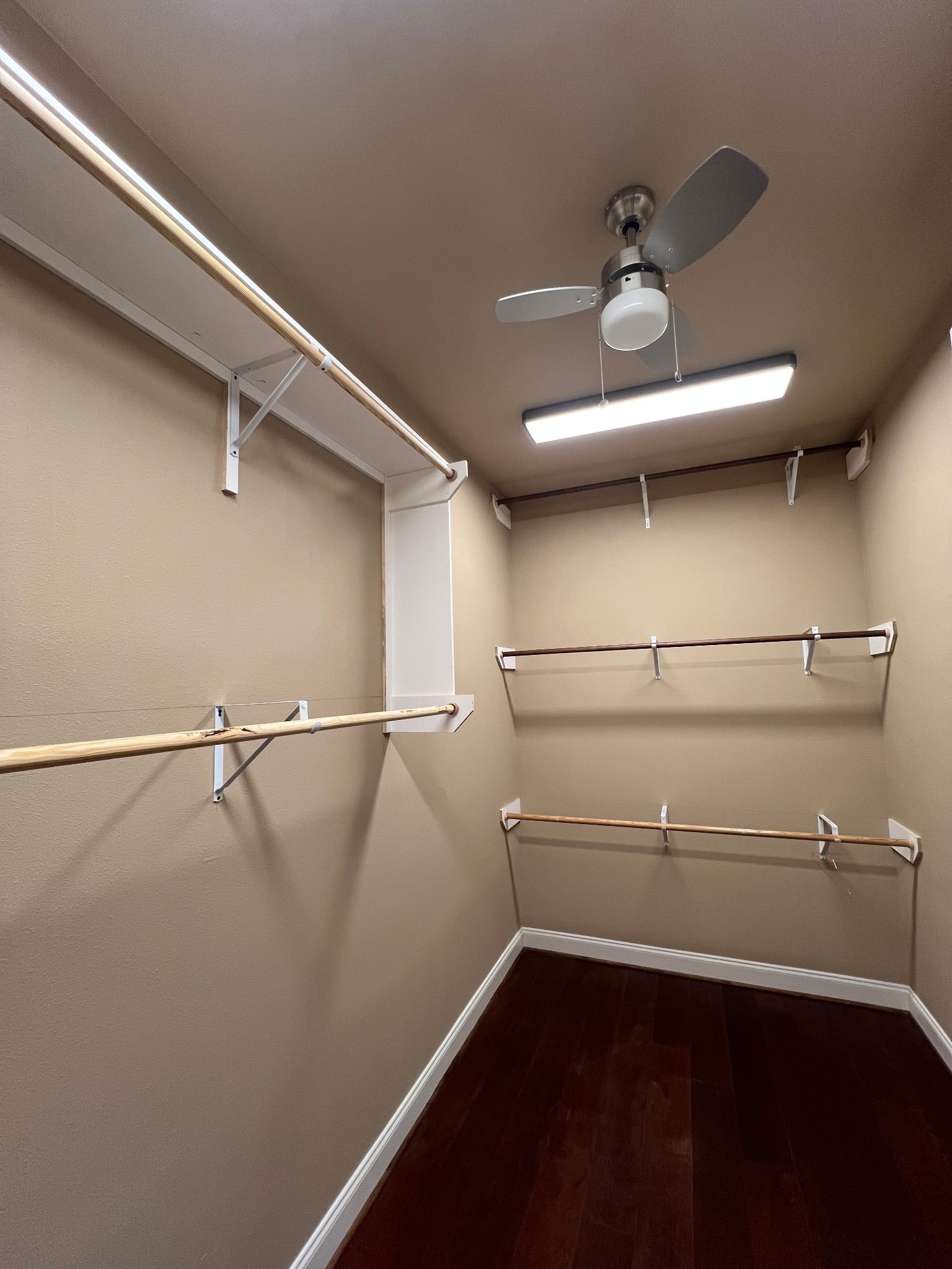 6315 Amelia Springs Drive Spring, TX 77379 - Photo 25 of 46 This is a spacious walk-in closet with ample wooden hanging rods, soft beige walls, and a sleek ceiling fan with overhead lighting. The dark hardwood floor adds warmth and elegance.