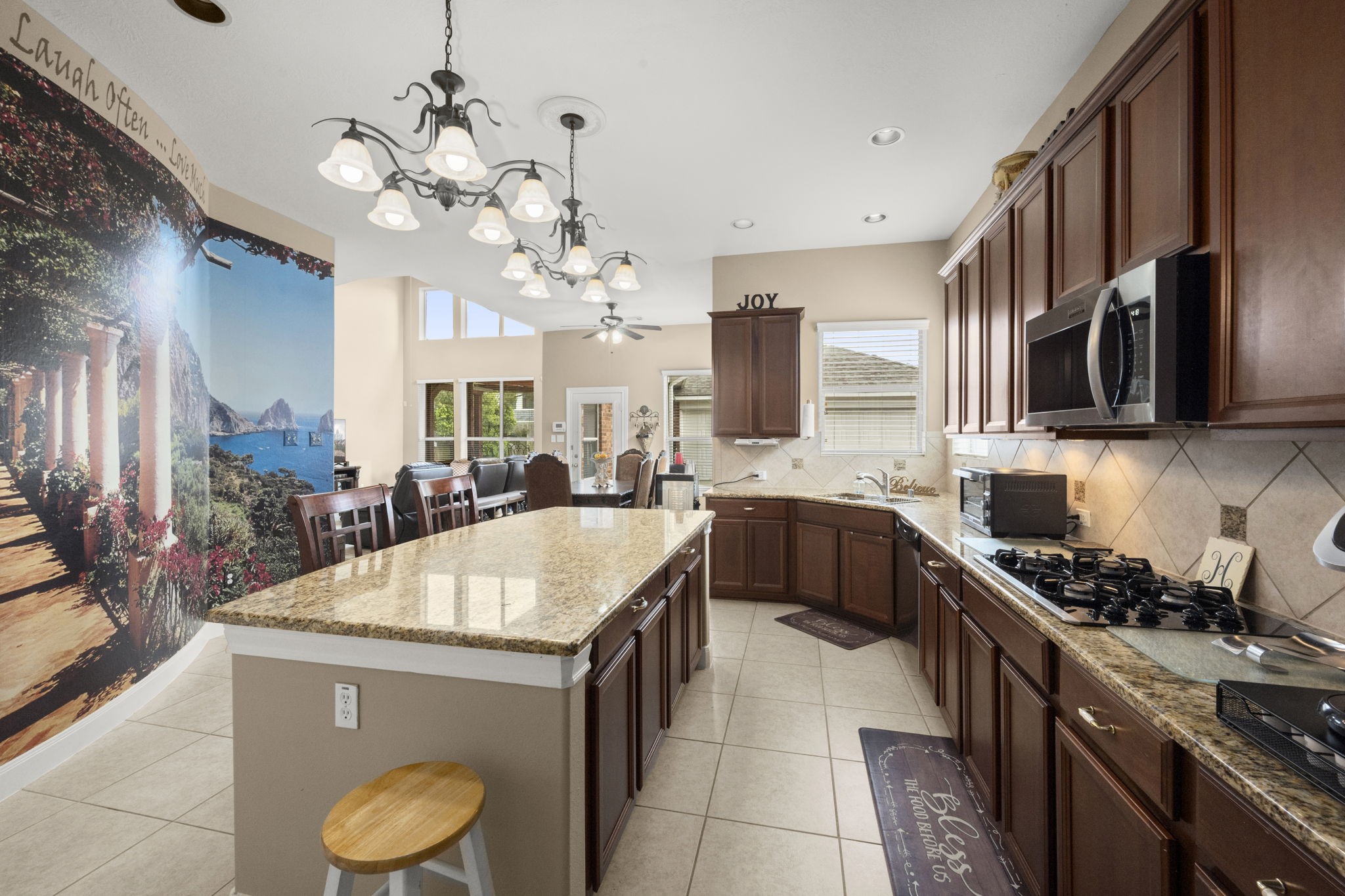 6315 Amelia Springs Drive Spring, TX 77379 - Photo 33 of 46 Kitchen features granite countertops, dark wood cabinetry, and stainless steel appliances. It has a large island with seating, tile flooring, creating a warm and inviting space for cooking and entertaining.