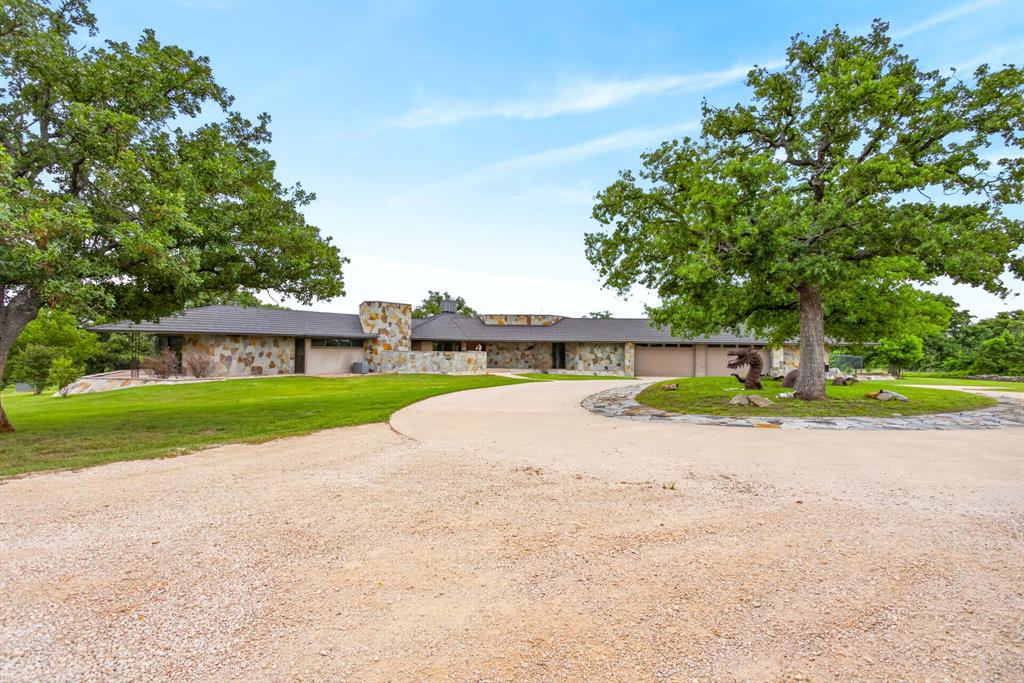 1080 North Greenbrier Road Nocona, TX 76255 - Photo 3 of 40 Ranch-style residence featuring a natural stone exterior, a gravel driveway, and a circular stone-edged island