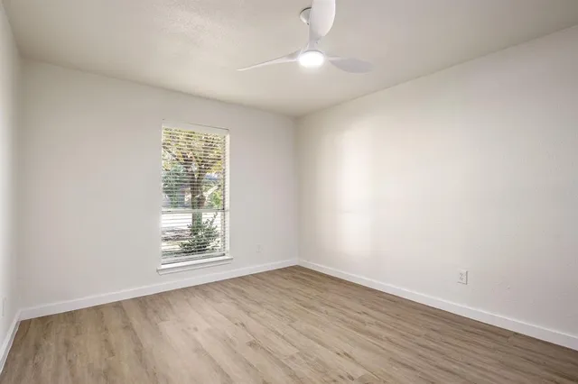 an empty room with wooden floor chandelier fan and windows