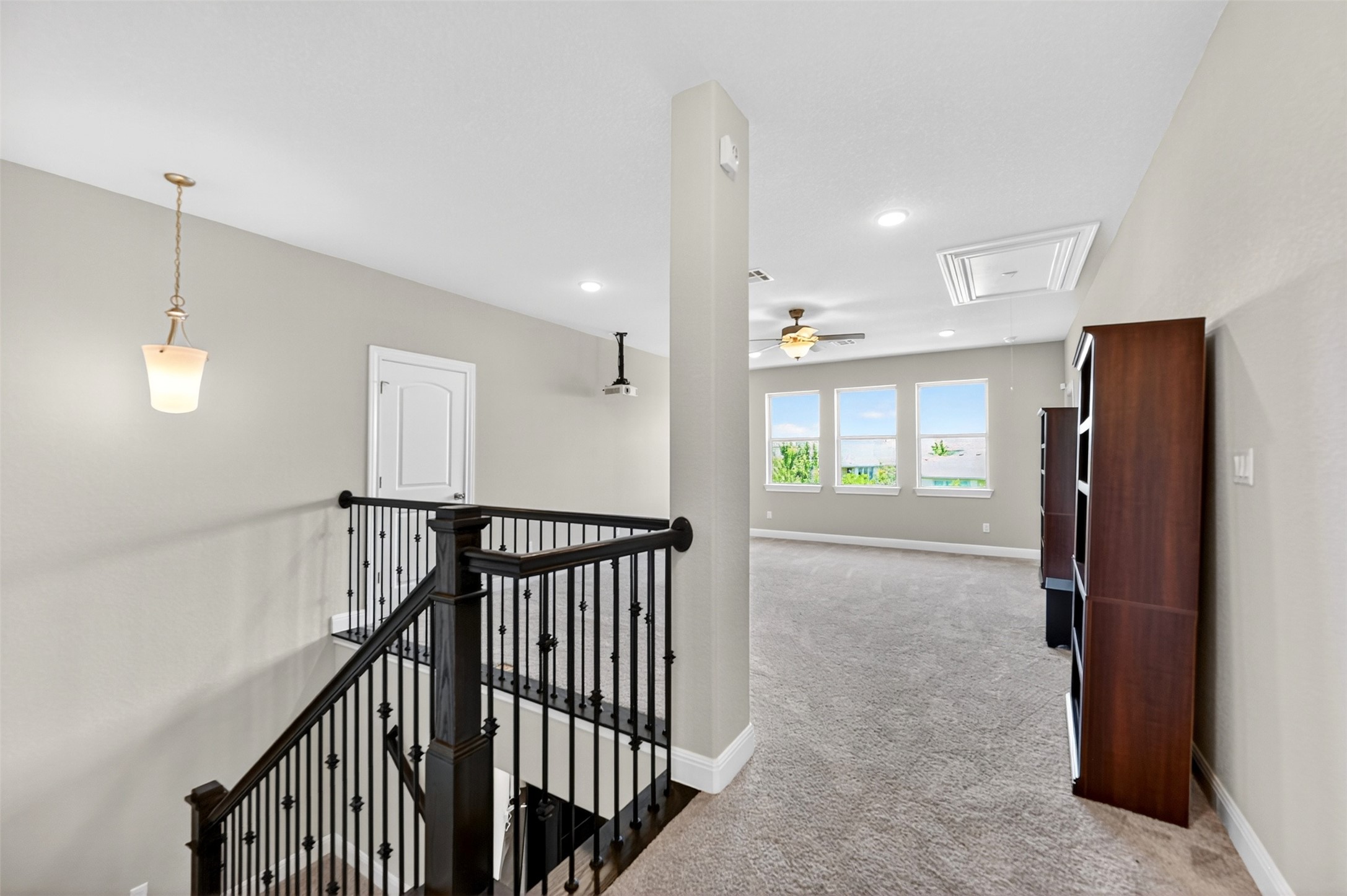 1201 Positano Pass Leander, TX 78641 - Photo 33 of 40 Carpeted second-story landing featuring dark wood stair railing with black iron spindles, ceiling-mounted light fixtures, white trim, and a white interior door