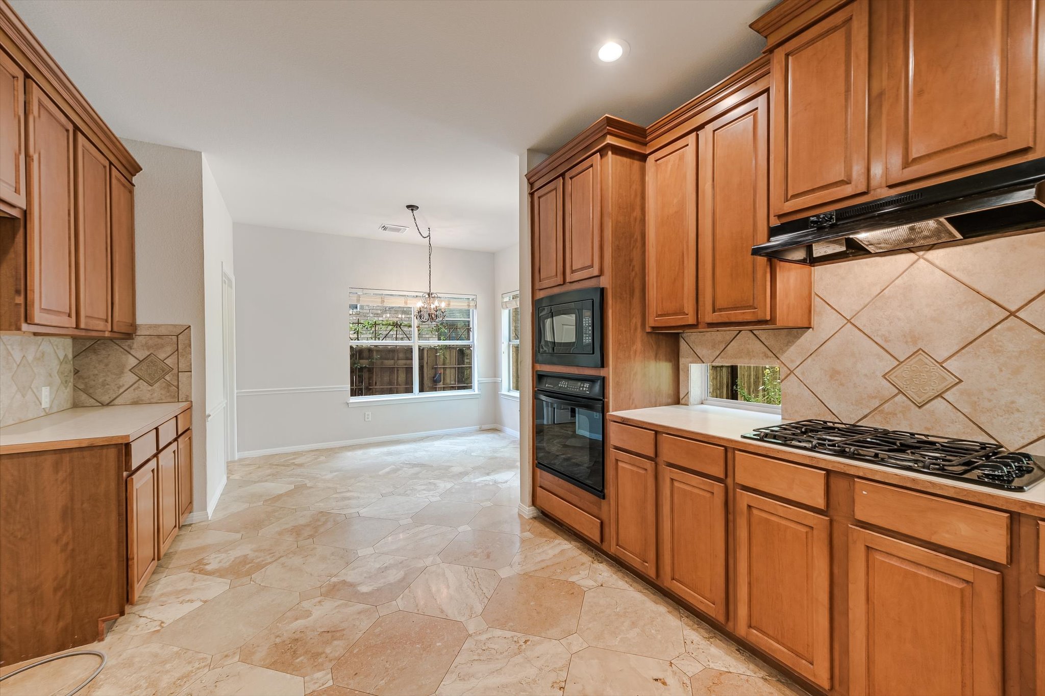 2849 Grimes Ranch Road Austin, TX 78732 - Photo 12 of 31 A well-equipped kitchen features honey-toned cabinetry, built-in appliances, and natural stone tile flooring.
