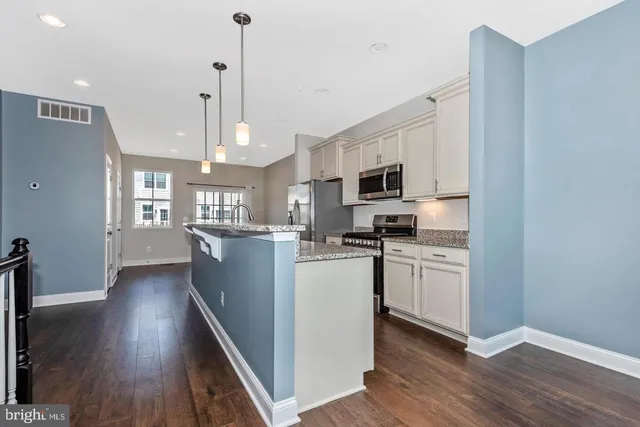 a kitchen with stainless steel appliances granite countertop a refrigerator a sink dishwasher a stove and a wooden floor