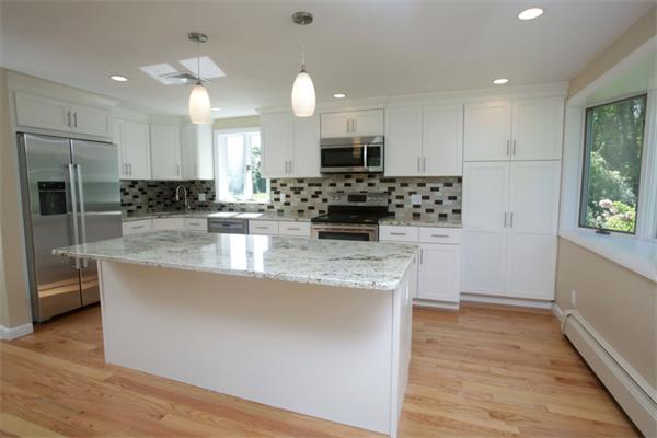 a kitchen with kitchen island granite countertop a stove a sink a refrigerator and white cabinets with wooden floor