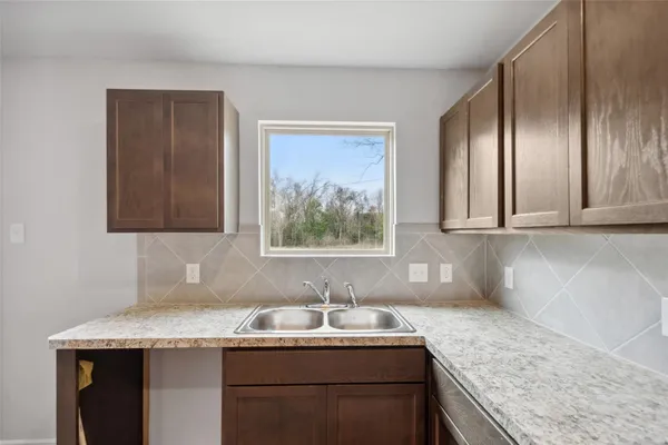 a kitchen with a granite countertop sink a window and cabinets