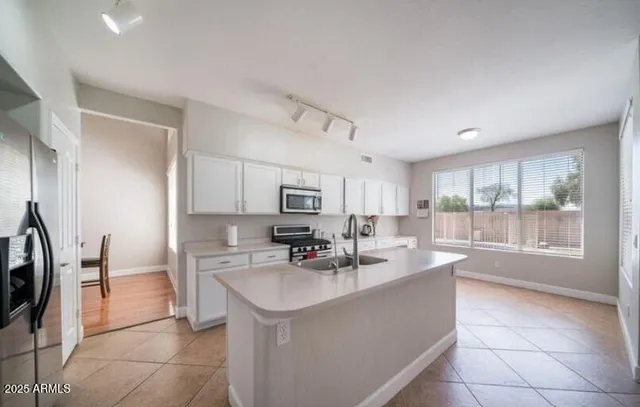 a kitchen with stainless steel appliances a sink a stove a refrigerator cabinets and a dining table with wooden floor