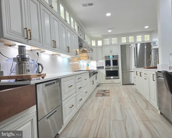 a kitchen with stainless steel appliances granite countertop a refrigerator oven a sink dishwasher and white cabinets with wooden floor