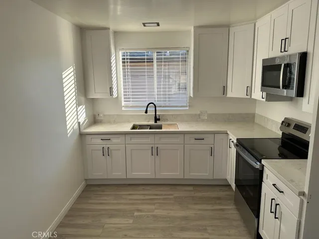 a kitchen with granite countertop a sink white cabinets and stainless steel appliances