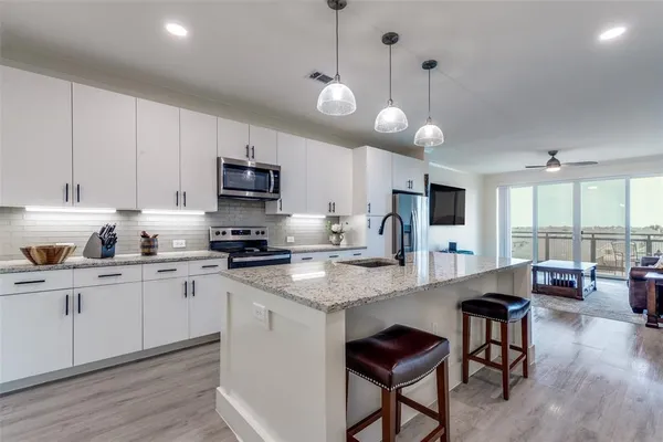 a kitchen with stainless steel appliances granite countertop a stove top oven a sink a dining table and chairs with wooden floor