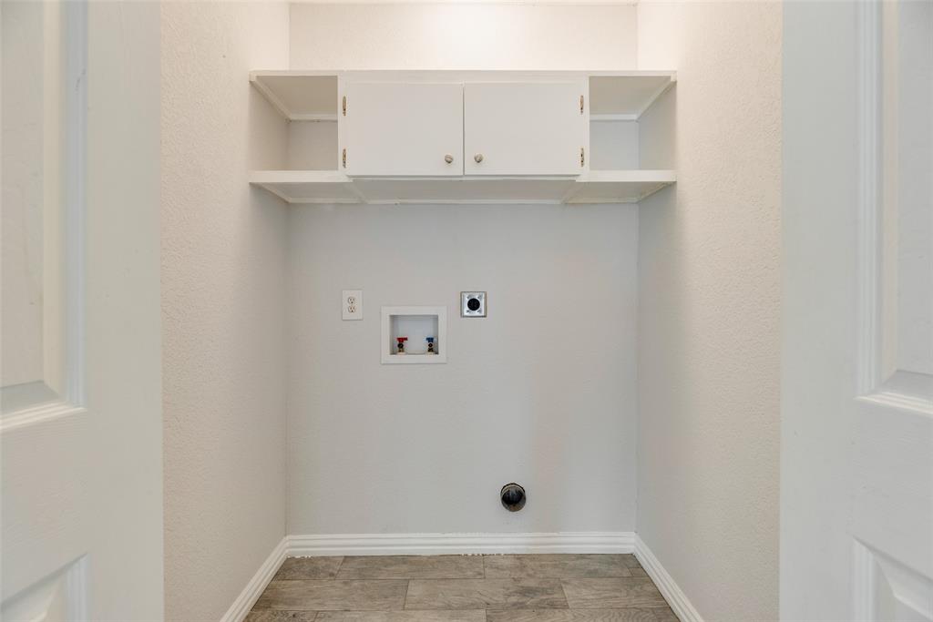 5109 Cedar Springs Road, Unit 105 Dallas, TX 75235 - Photo 9 of 16 Dedicated laundry area featuring overhead white cabinetry with silver hardware, open shelving, and wood-finish flooring