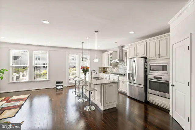 a kitchen with stainless steel appliances kitchen island granite countertop a refrigerator a stove a sink a dining table and chairs with wooden floor