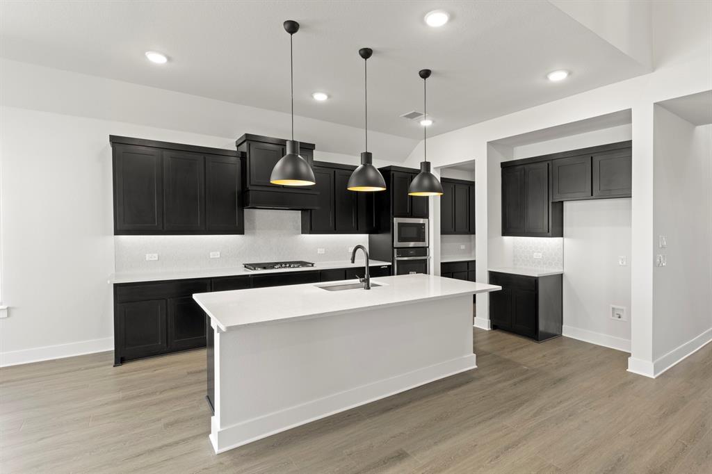 2917 Andesite Road McKinney, TX 75071 - Photo 7 of 27 a large kitchen with stainless steel appliances kitchen island a large counter top space a sink and a wooden floor